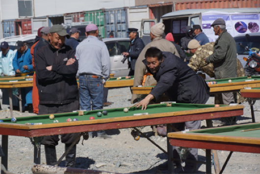 A group of locals play pool in the town square. The van can be spotted behind them.
