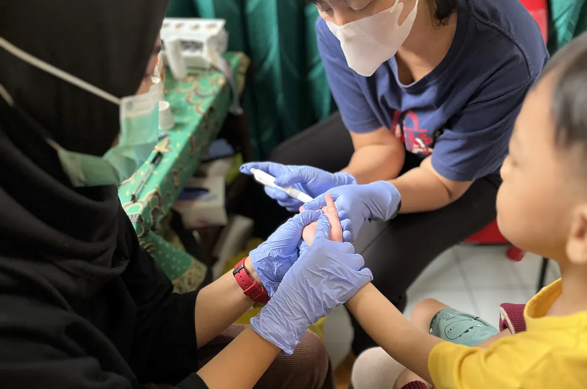 A health worker tests a child’s blood lead level in Indonesia.